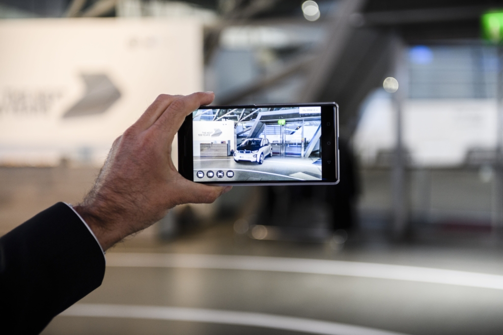 Das Bild zeigt eine Hand, die ein Mobiltelefon hält, auf dem ein Augmented-Reality-Modell eines BMW im Raum zu sehen ist.